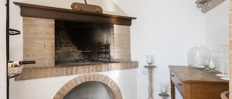 Una chimenea de ladrillo con repisa, una mesa de madera con cristalería y un piso de baldosas.