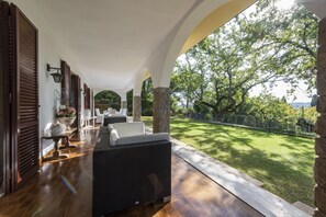 Un espace extérieur aménagé, abrité et doté de mobilier en osier, de piliers en pierre et offrant une vue sur une pelouse bien entretenue.