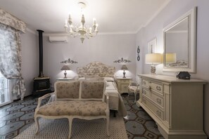 Ein Schlafzimmer mit einem Bett, zwei Nachttischen mit Lampen, einem Schminktisch, einem Stuhl, einer Chandelieber, einem Spiegel und einem Fenster mit Vorhängen.