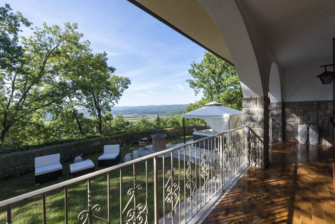 Un balcon donnant sur un paysage verdoyant, un mur de pierre et un parasol blanc.