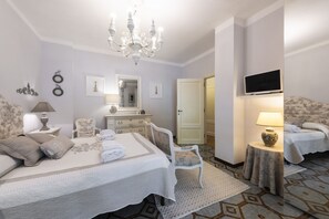 Una camera da letto con un letto, due poltrone, una televisione, un lampadario e una porta.