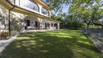Una casa a due piani con facciata in pietra, ampie finestre e un prato curato.