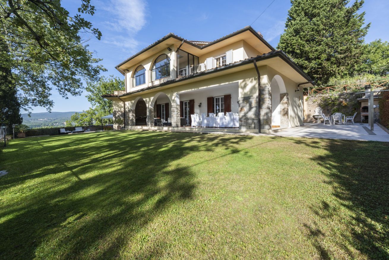 Una grande casa a due piani con un ampio prato anteriore, colonne in pietra e un balcone che si affaccia sul paesaggio.