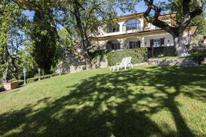 Ein zweistöckiges Haus mit großem Rasen, einem weißen Stuhl und einem Baum im Vordergrund.