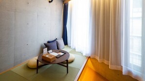 Una habitación con suelo de tatami, una mesa baja con cojín, un control remoto y una pequeña caja de madera.
