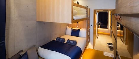Habitación de hotel compacta con una cama litera, una cama individual y un pequeño rincón de descanso.