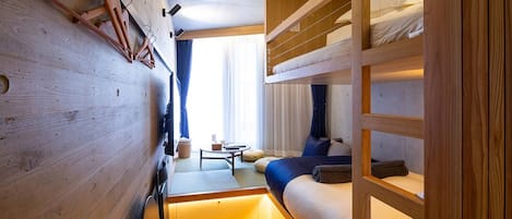 Una habitación de hotel pequeña con literas, una mesita y un sofá.