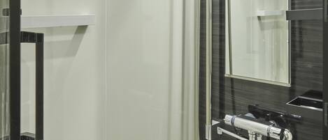 A modern bathroom with a glass shower enclosure, a handheld showerhead, a wall-mounted faucet, and a large mirror.