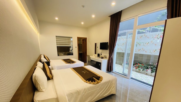 Habitación de hotel con dos camas, un escritorio, un televisor y un amplio ventanal con vistas a un jardín.