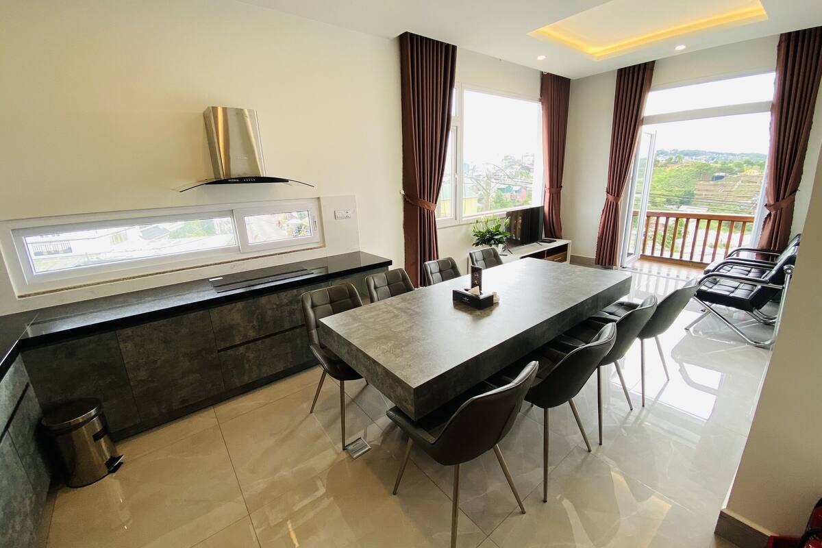 A modern kitchen with a built-in stove, a dining area with a large table and chairs, and a view of the outdoors through large windows.