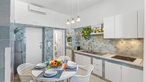 A modern kitchen with white cabinets, a blue tiled backsplash, and a dining area with white chairs and a table set for four. - Seaview Home on the beach & amazing views terrace (Sorrento)