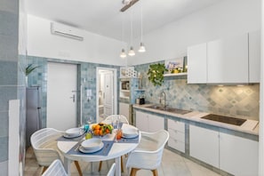 A modern kitchen with white cabinets, a blue tiled backsplash, and a dining area with white chairs and a table set for four. - Seaview Home on the beach & amazing views terrace (Sorrento)