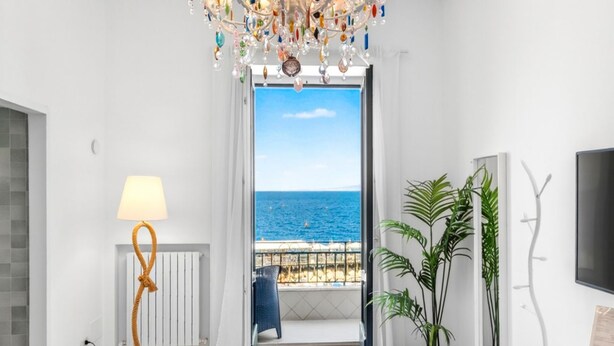 A room with a view of the sea, a chandelier, a lamp, a potted plant, and a TV. - Seaview Home on the beach & amazing views terrace (Sorrento)
