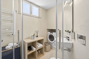 A compact bathroom with a washing machine, a sink, and a mirror.