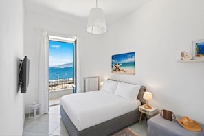 A bedroom with a bed, a nightstand, a lamp, a suitcase, and a hat.