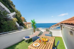 A balcony with a table set for two, a plate of food, and a fruit bowl.