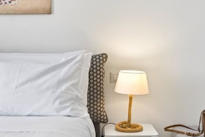 A neatly made bed with white bedding, a patterned pillow, a round table lamp with a rope base, and a brown leather bag on the side. - Seaview Home on the beach & amazing views terrace (Sorrento)
