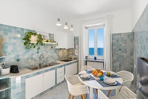 A kitchen with a dining area, a view of the sea, and a window with curtains.