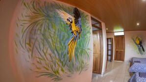 Ein Zimmer mit einer Wandmalerei von Vogel und Grünpflanzen, Holztüren und einem Bett mit gemusterten Bettwäsche.