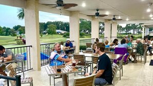 Ein Außenbereich mit Essbereich, Tischen und Stühlen, mit Blick auf einen Golfplatz und einem überdachten Bauwerk.