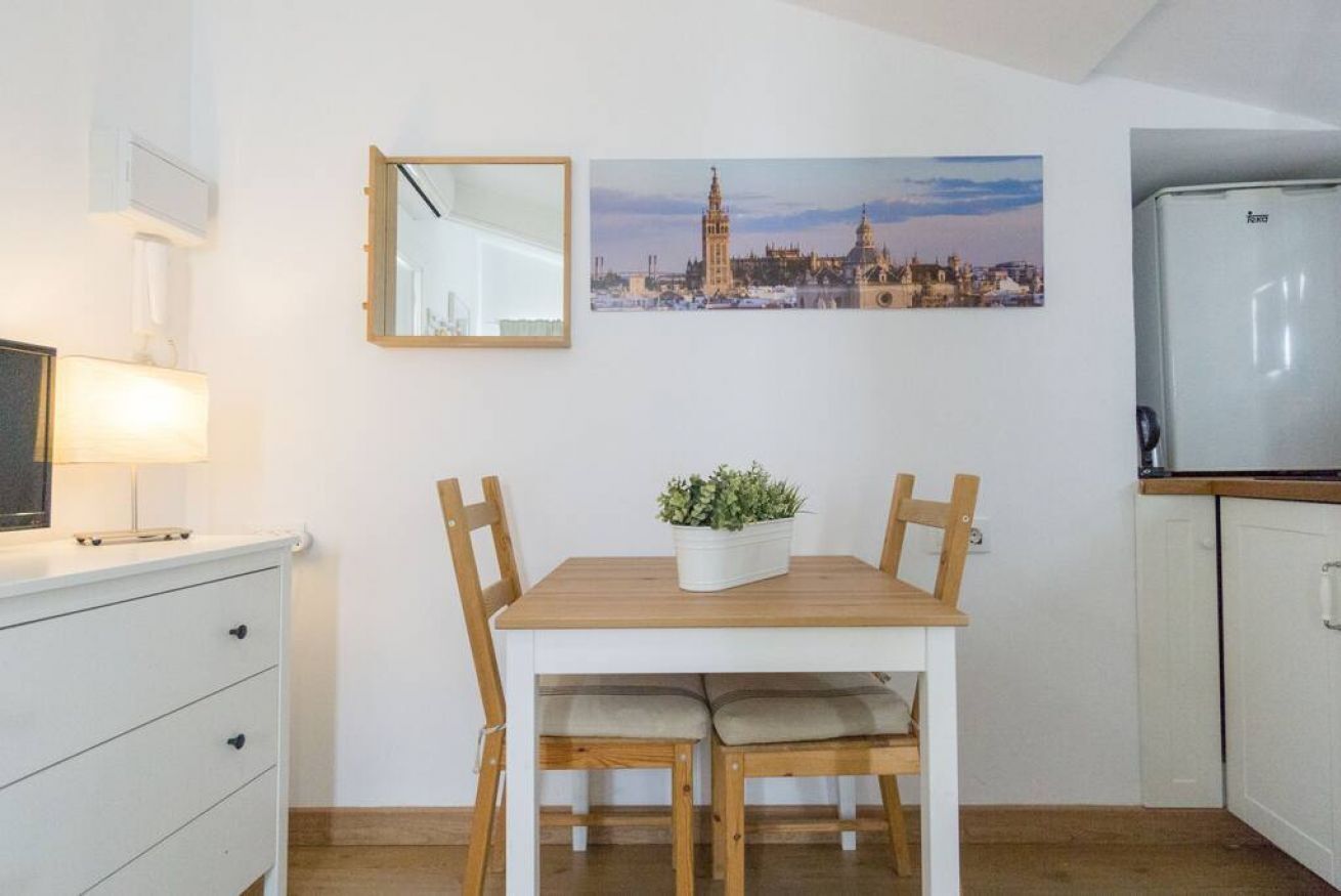 Une cuisine compacte comprenant une table à manger, des chaises, un réfrigérateur, un miroir et un tableau représentant un paysage urbain.