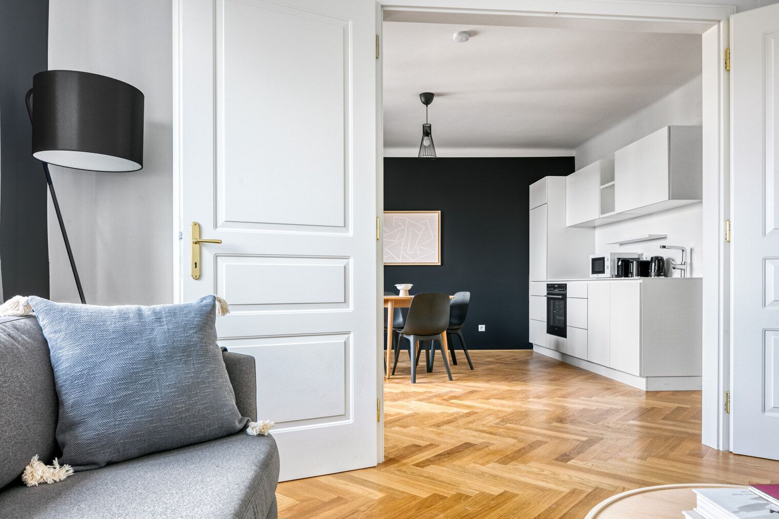A modern living room with a grey sofa, a black floor lamp, and a dining area with a table and chairs.