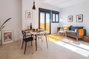 A modern living room with a sofa, a dining table with chairs, and a balcony with large windows. - Housing Ollerias by Sharing Co (Málaga)