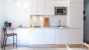 Una cocina moderna con armarios blancos, un microondas integrado y una tabla de cortar de madera.