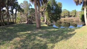A grassy area with a pond and trees, and a small building with a yellow roof.
