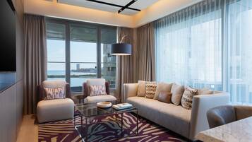 Una habitación de hotel moderna con un sofá, sillones, una mesa de centro de vidrio y vistas a la ciudad.