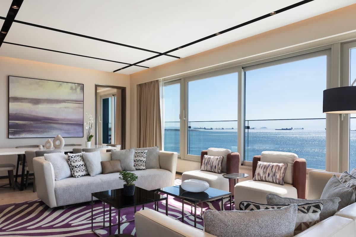 Un salón moderno con un ventanal grande, un conjunto de sofás, una mesa de centro y vista al mar.