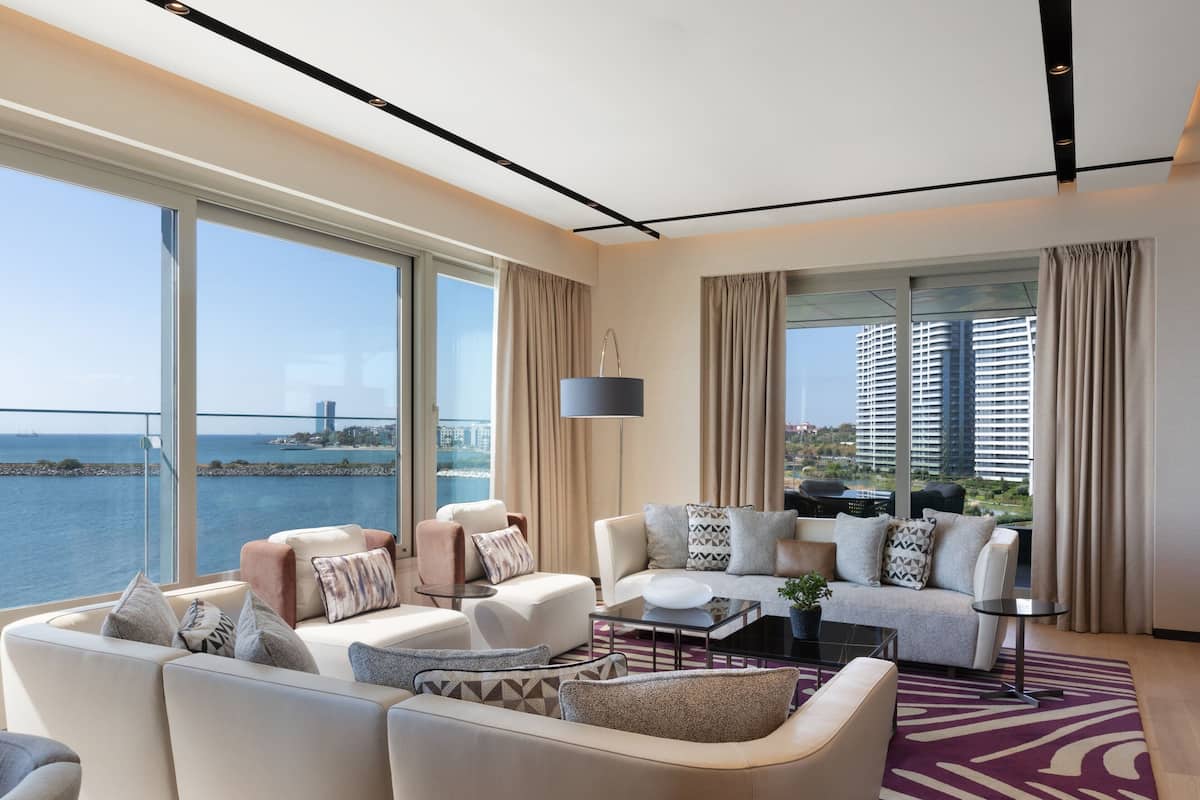 Salón moderno con un ventanal grande que da a una masa de agua y edificios, amoblado con sofás y una mesa de centro.