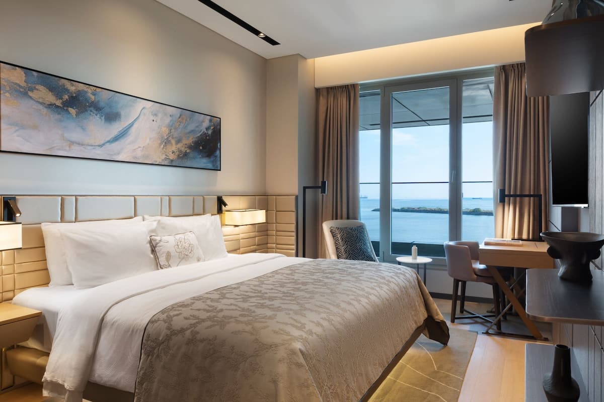 Habitación de hotel moderna con una cama grande, un escritorio y vista al mar.