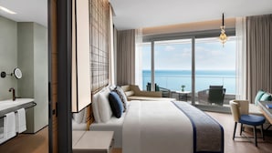Habitación de hotel moderna con una cama grande, un escritorio, una silla, vistas al mar y un balcón.