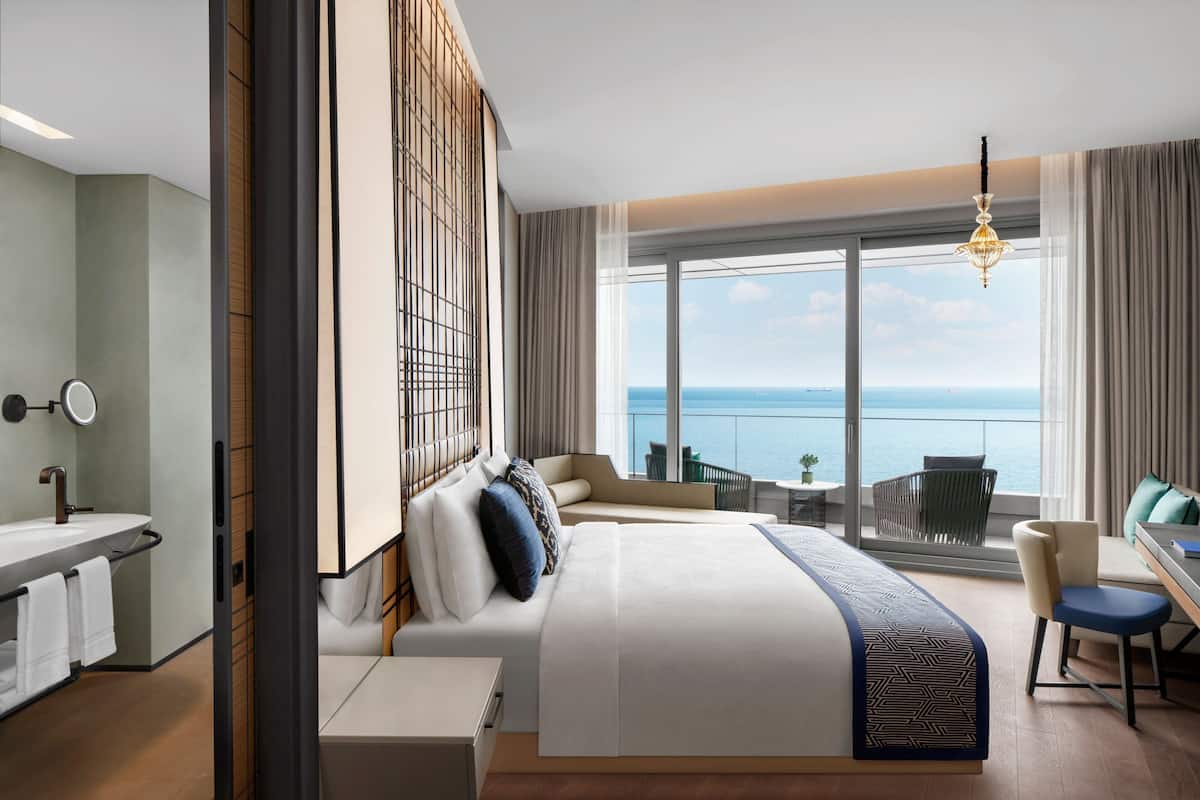 Habitación de hotel moderna con una cama grande, un escritorio, una silla, vistas al mar y un balcón.