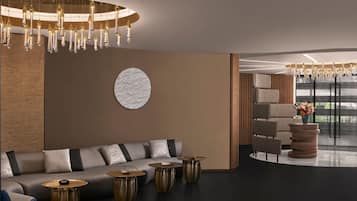 A modern lobby with a sofa, round tables, and a large chandelier.