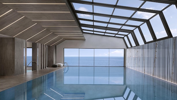 Una piscina interior moderna con un amplio tragaluz y vistas al mar.