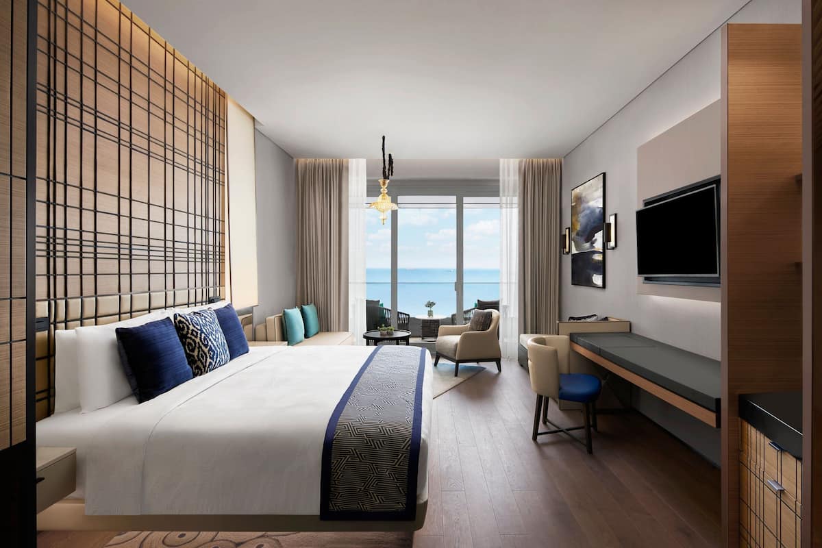 Una habitación de hotel moderna con una cama grande, un escritorio, un televisor y vistas al mar.