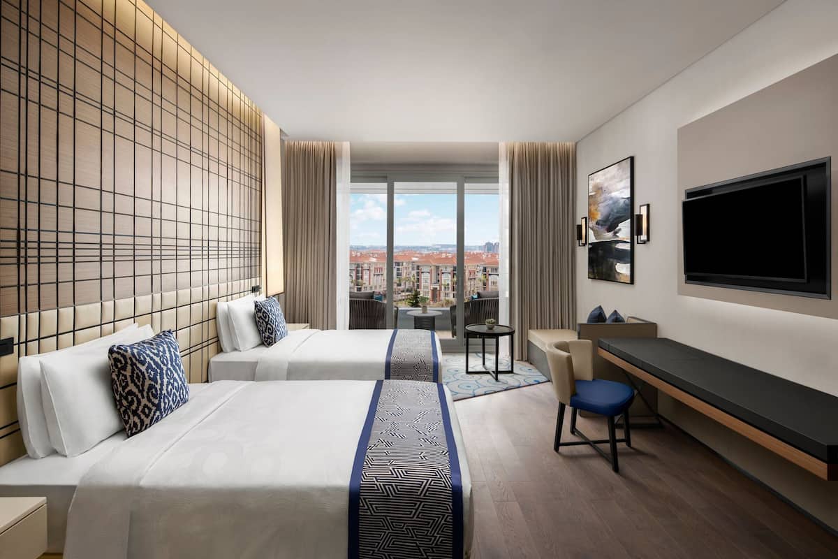 Una habitación de hotel con dos camas, un escritorio, un televisor y vista a la ciudad.