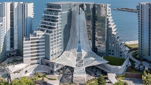 Un hotel moderno con una fachada geométrica distintiva, varios balcones y un atrio central con techo de cristal.