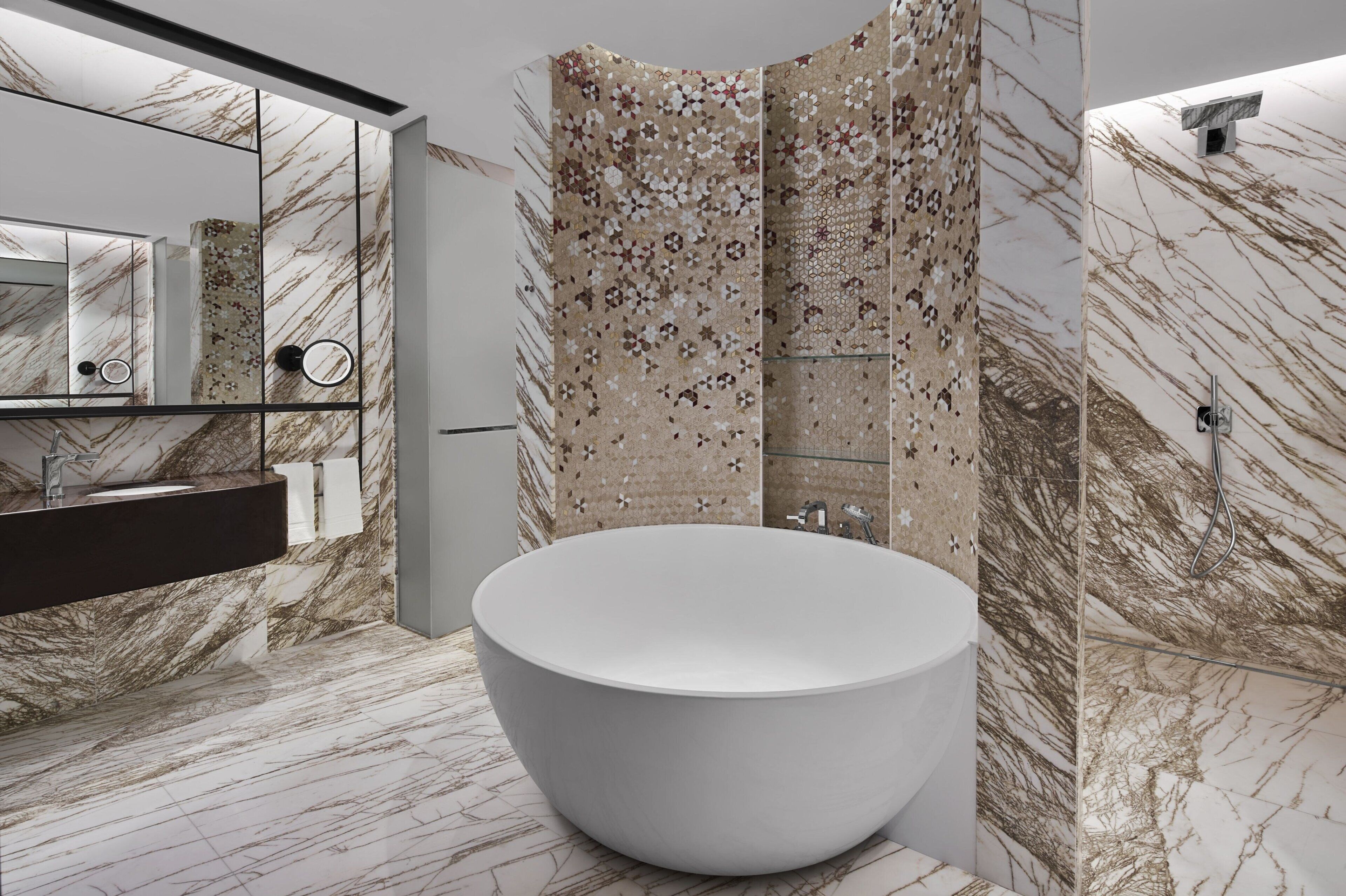 Un baño moderno con una bañera independiente grande, cabina de ducha con mampara de vidrio y pared con azulejos de mármol.
