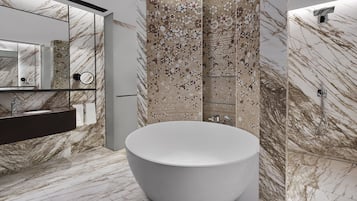 Un baño moderno con una bañera independiente grande, cabina de ducha con mampara de vidrio y pared con azulejos de mármol.
