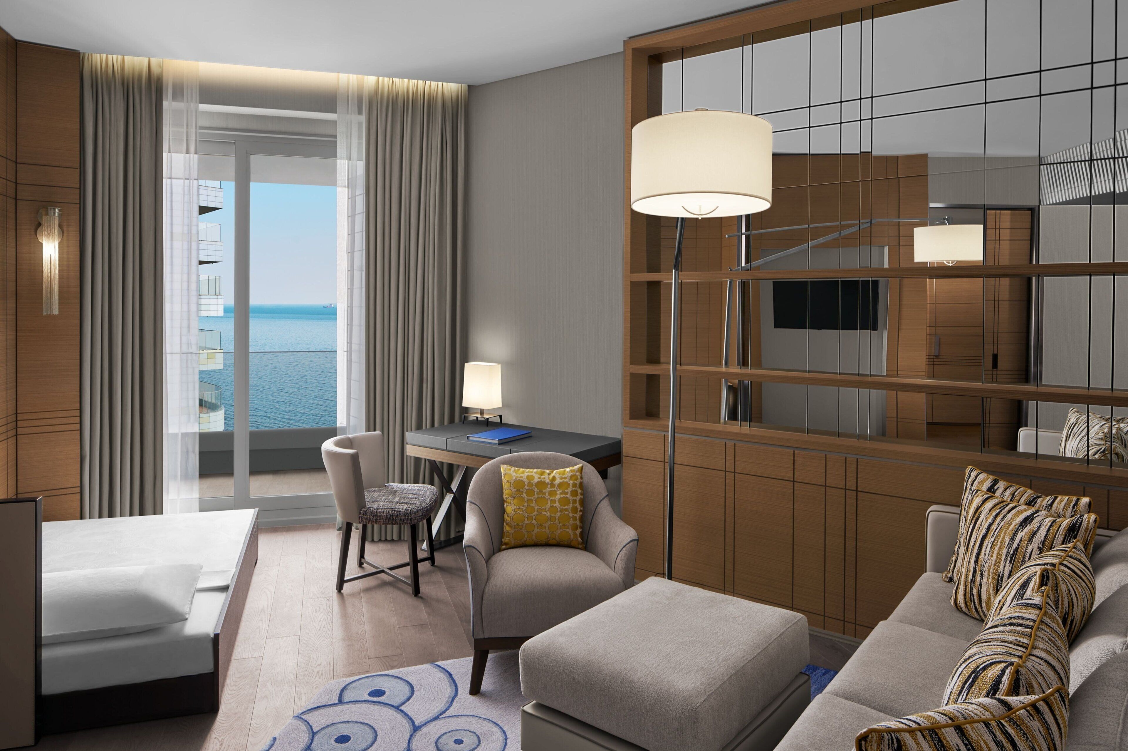 A modern hotel room with a balcony, a desk, a sofa, and a TV.