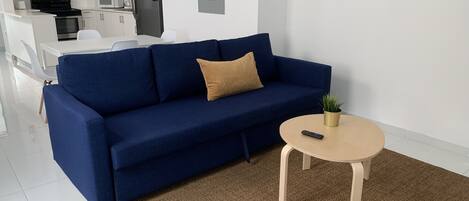 A modern living room with a blue sofa, a small round table, and a remote control on the table.