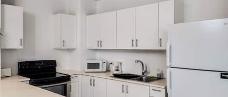 Een keuken met witte kasten, een zwarte kookplaat, een magnetron, een spoelbak en een koelkast.