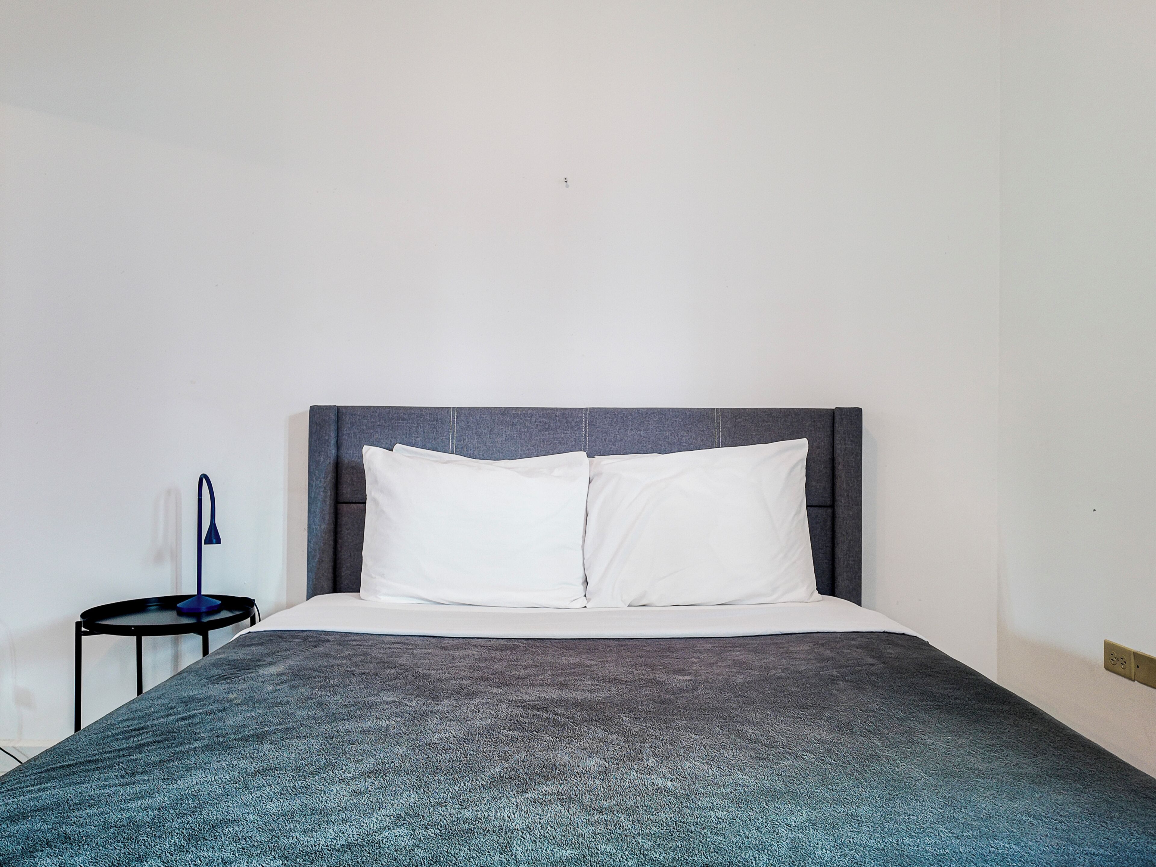 A bed with a grey headboard, white pillows, and a grey blanket.