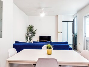 Un salon moderne avec une table blanche, un canapé bleu, un ventilateur de plafond et une petite plante en pot.