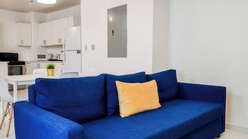 Ein modernes Wohnzimmer mit einem blauen Sofa, einem gelben Kissen und einer Küche im Hintergrund.