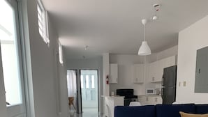 Ein modernes Wohnzimmer mit einem blauen Sofa, einem braunen Teppich und einer Küchenzeile mit weißen Schränken und Geräten.