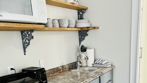 Cocina equipada con microondas, tostadora y lavavajillas. Hay repisas sobre la encimera con vajilla y una cafetera.